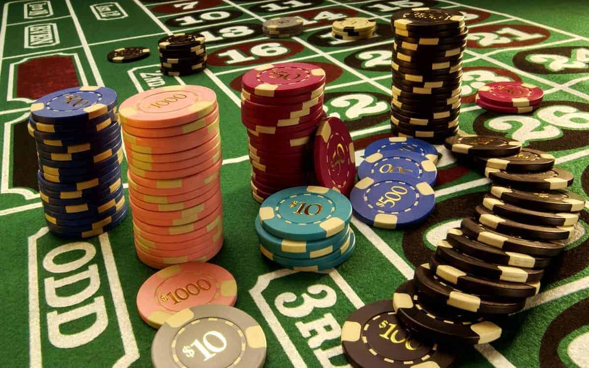 ชิปคาสิโนหลากสีวางซ้อนเป็นกองบนโต๊ะพนันสีเขียว ภาพประกอบที่ 1
