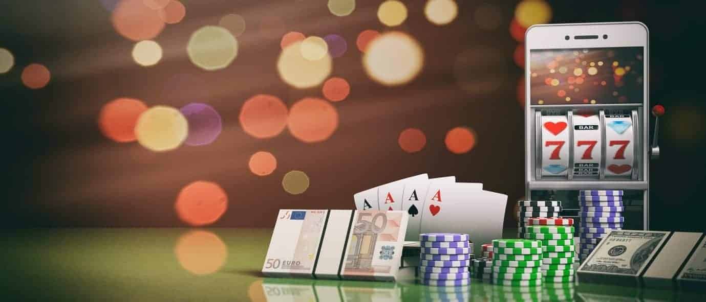 มือถือแสดงสล็อต 777 วางข้างไพ่เอซ กองชิป และธนบัตรยูโรกับดอลลาร์