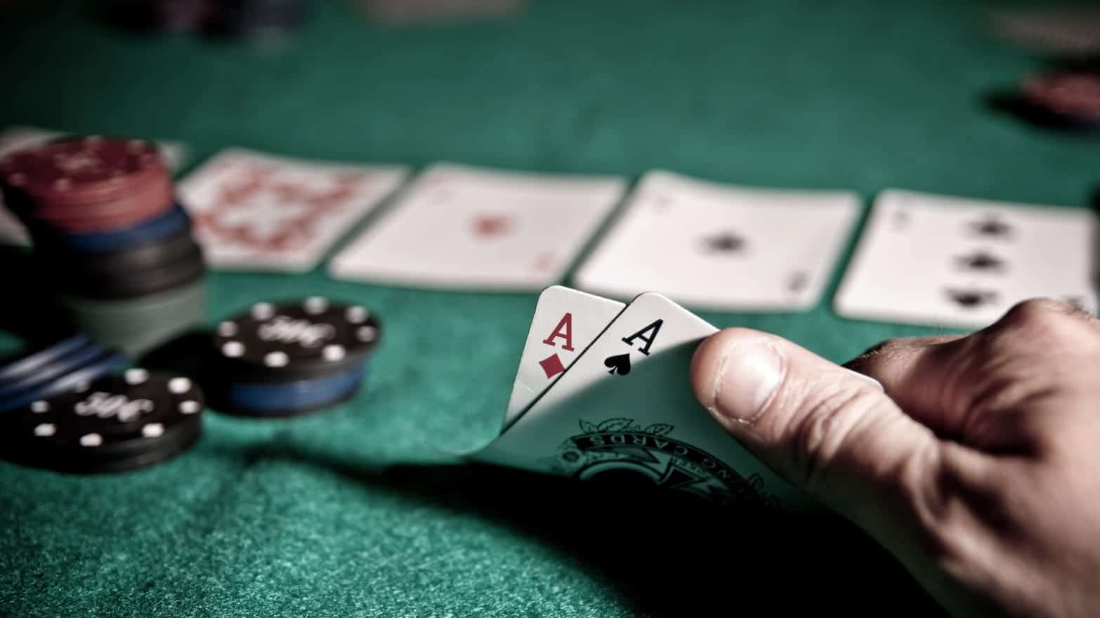 มือเปิดไพ่เอซสองใบบนโต๊ะสักหลาดเขียวข้างกองชิป